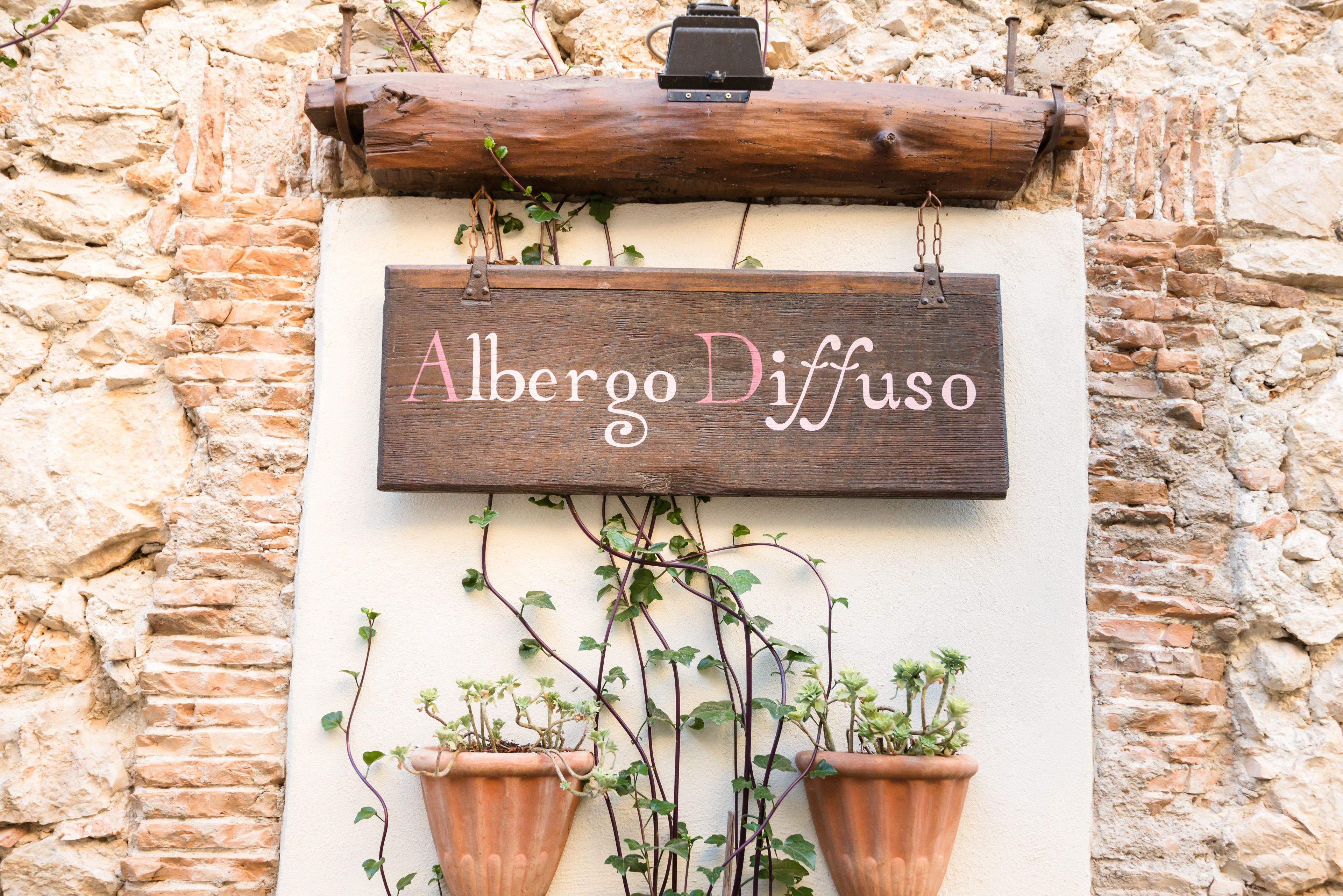 A rustic wooden sign with the name "Alberto Diffuso" hanging on a stone wall.