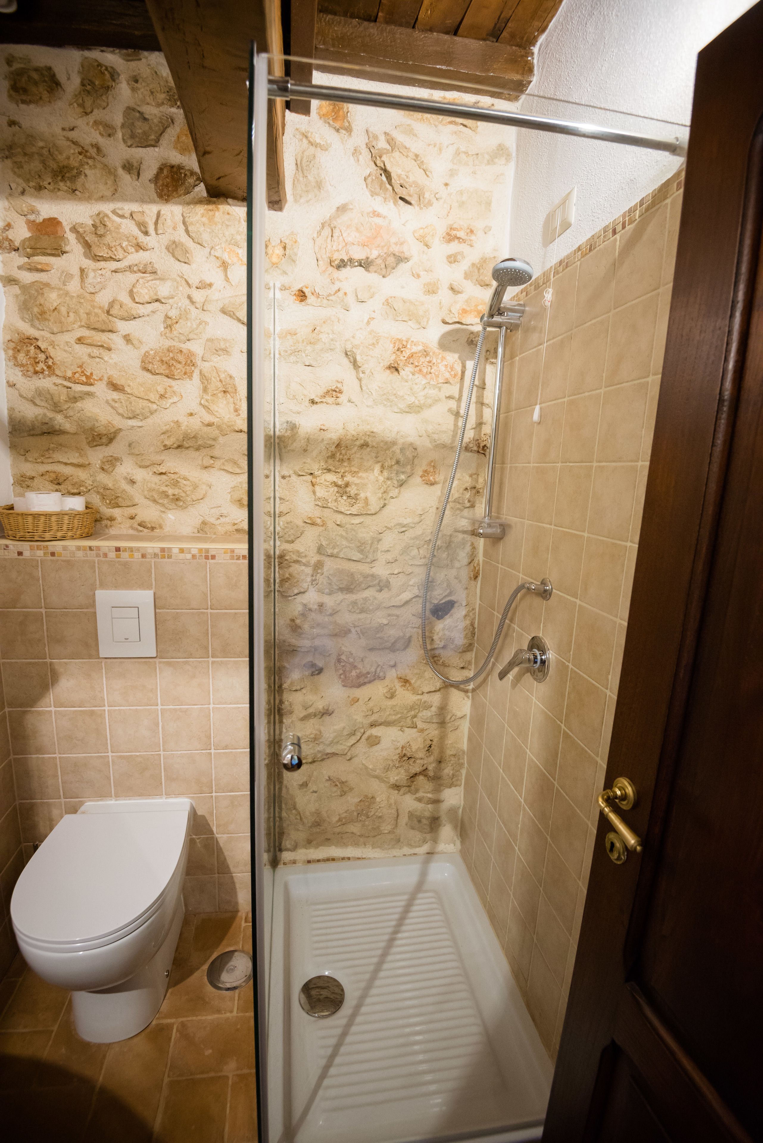 A bathroom with a stone wall, a shower, a toilet, and a door.