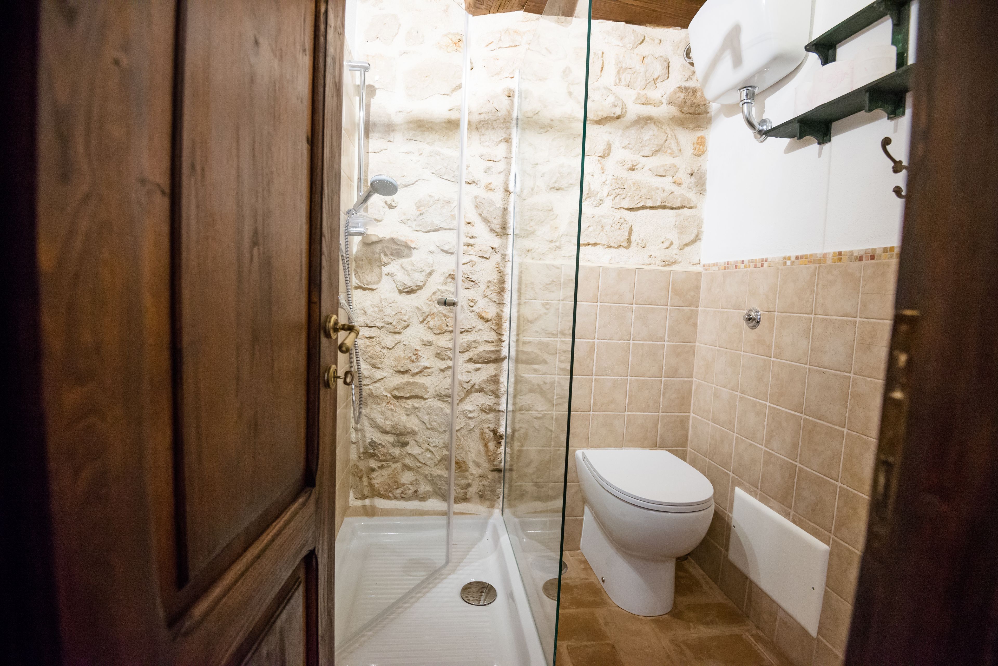 Une salle de bain avec un mur en pierre, une douche en verre, des toilettes et une baignoire.