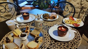 A table set with various dishes including bread, pastries, and a fruit bowl, with a woven placemat and a view of a stone wall and plants in the background. - Nena' al Borgo Castello (Pico)