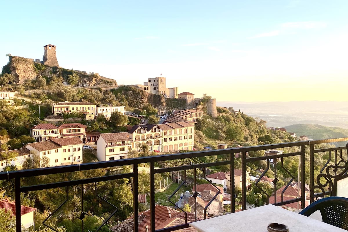 A balcony with a table and chairs overlooking a hillside with buildings and a castle.
