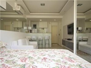 Een moderne hotelkamer met een groot bed, een zithoek met een bank en stoelen, een kitchenette en een televisie.