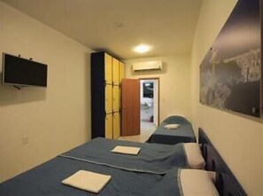 A narrow hotel room with two beds, a TV, and a painting on the wall.