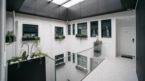 A modern interior with a glass railing, white walls, and multiple windows with plants. - D'Autor Apartments (Porto)