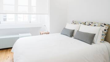 A modern bedroom with a large bed, a bedside table, and a window with blinds.