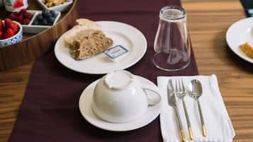 Una mesa dispuesta con tetera, un plato de pan y una etiqueta, una jofaina de vidrio y una servilleta con cubiertos.