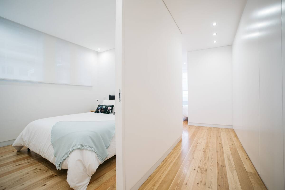 A modern bedroom with a wooden floor, a bed with a light blue blanket, and a white wall.