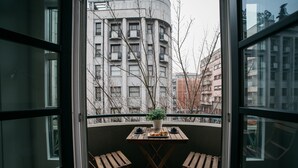 A balcony with a wooden table and two chairs, a potted plant, and a view of a multi-story building. - D'Autor Apartments (Porto)