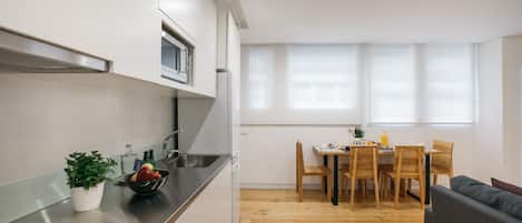 A modern kitchen with a dining area, wooden flooring, and a large window providing natural light.