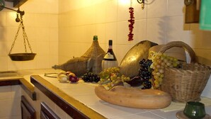 A kitchen counter with a scale, a bottle, a basket of grapes, and a large sausage. - Agriturismo Santa Caterina (Castelnuovo di Val di Cecina)