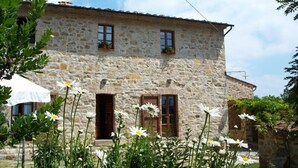 A stone building with two windows and a door, surrounded by white flowers. - Agriturismo Santa Caterina (Castelnuovo di Val di Cecina)