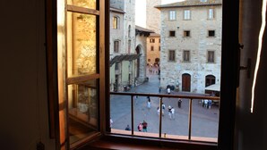 A view from a window overlooking a courtyard with stone buildings, a railing, and people walking. - B&B Ridolfi (San Gimignano)