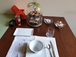 A neatly arranged table with a glass dome containing pastries, a white plate, a glass, a spoon, and a napkin. - B&B Ridolfi (San Gimignano)