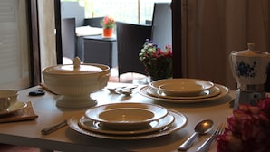 A dining table set with white plates, bowls, and cutlery, with a view of an outdoor patio in the background. - B&B Ridolfi (San Gimignano)