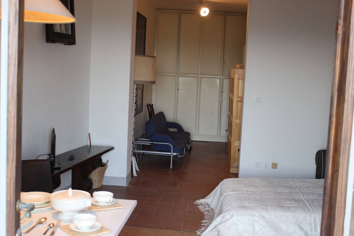 A bedroom with a bed, bedside table, and a chair. There is a desk with a lamp and a chair in the corner.