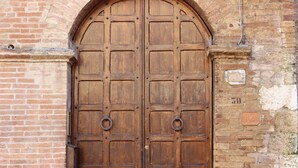 A large wooden double door with metal rings, set in a brick wall with a number plaque. - B&B Ridolfi (San Gimignano)