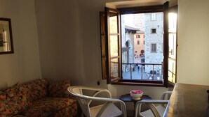 A room with a floral sofa, two white wicker chairs, a small table with a bowl, and a view of a street through a window. - B&B Ridolfi (San Gimignano)