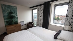 A hotel room with two beds, a wooden dresser, a chair, and a large window with a city view. - Cranbrook House Serviced Apartments (Nottingham)