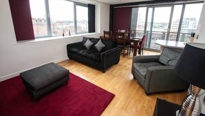 A modern living room with a sofa, ottoman, and dining area. - Cranbrook House Serviced Apartments (Nottingham)