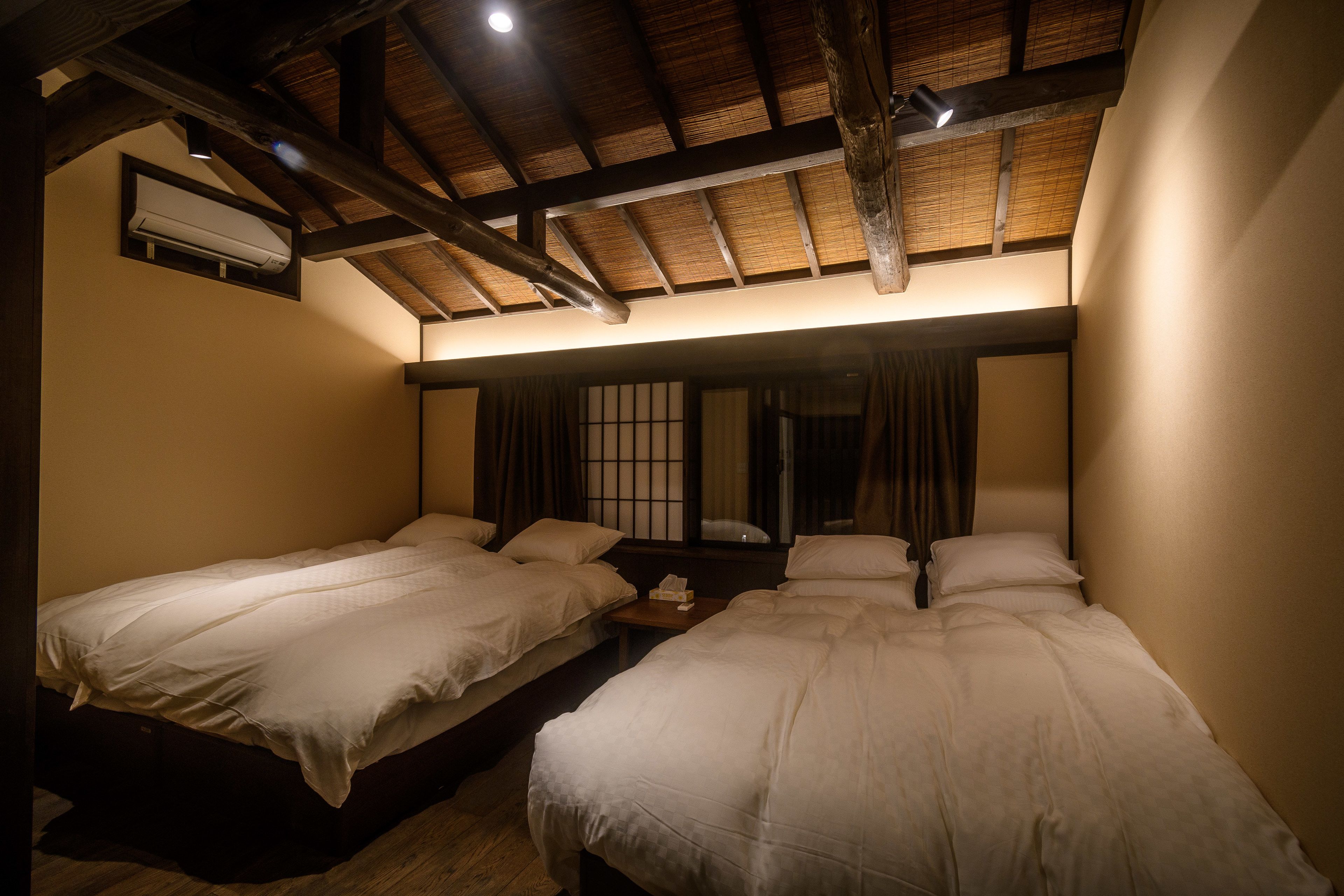 Una habitación con dos camas, vigas de madera en el techo y una ventana con cortinas.