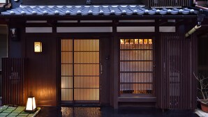 En traditionell japansk byggnad med ett tak täckt av tegelpannor, trädörrar med vertikala ribbor och en liten lykta placerad på marken.