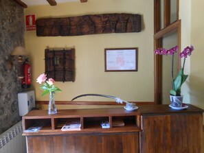 A reception desk with a vase of pink flowers, a framed certificate, and a wooden cabinet. - Hotel Rural Puente del Duraton (Sepulveda)
