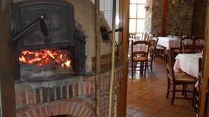 A brick oven with firewood, wooden utensils, and a stone wall. Tables and chairs are arranged in the dining area. - Hotel Rural Puente del Duraton (Sepulveda)