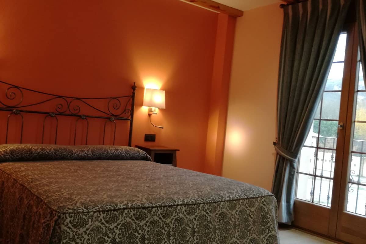 A bed with a patterned bedspread, two bedside lamps, a nightstand, and a window with curtains.