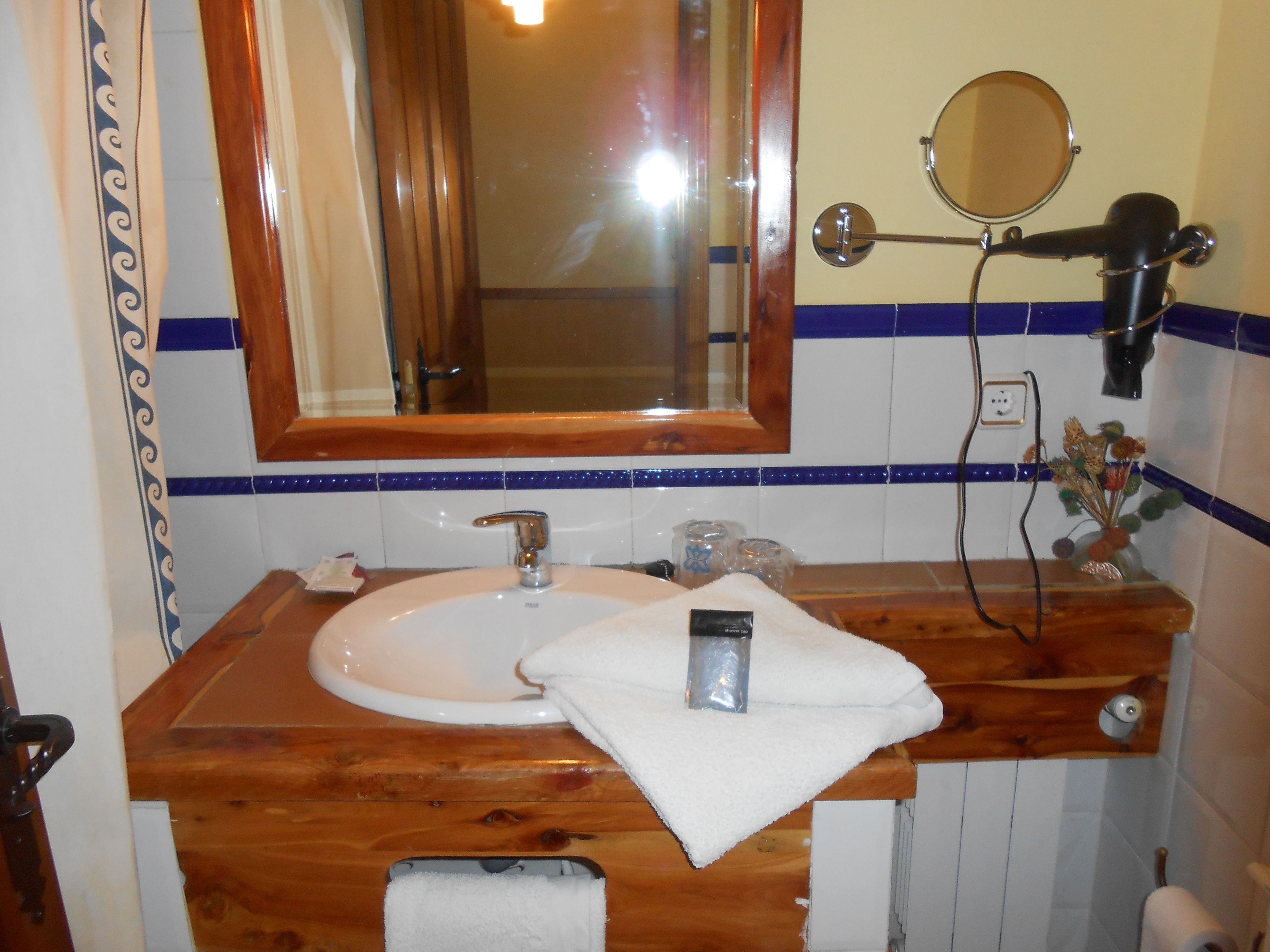 Un baño con tocador de madera, lavamanos blanco, espejo y secador de pelo en la pared.