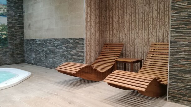 A spa area with two wooden loungers, a small table, and a hot tub. - Hotel Rural Puente del Duraton (Sepulveda)