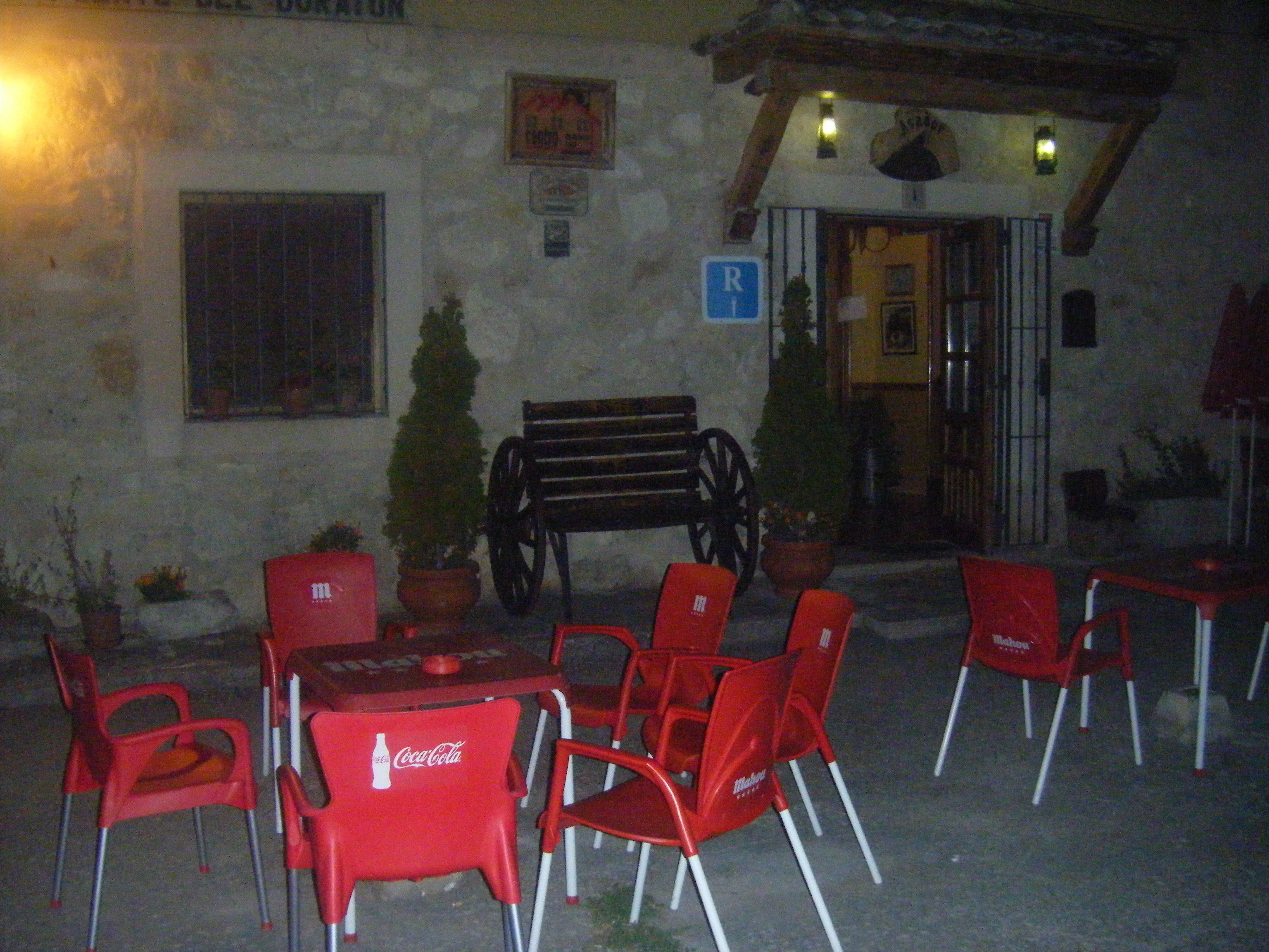 An outdoor seating area with red plastic chairs and tables, a wooden bench, and potted plants.