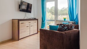 Una sala de estar moderna con un televisor de pantalla plana montado en la pared, un mueble de madera con cajones, un sofá marrón con cojines estampados y una ventana con cortinas azules.