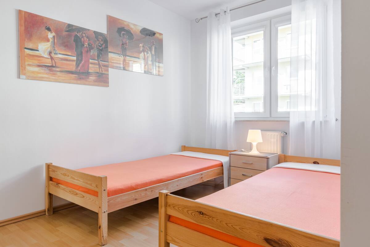 A room with two wooden beds, a nightstand, a lamp, and two paintings on the wall.