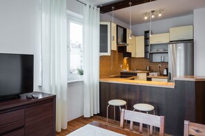 A compact kitchen with a TV, bar stools, and a built-in refrigerator. - Apartamenty Baltyckie - Na Wydmie (Ustka)