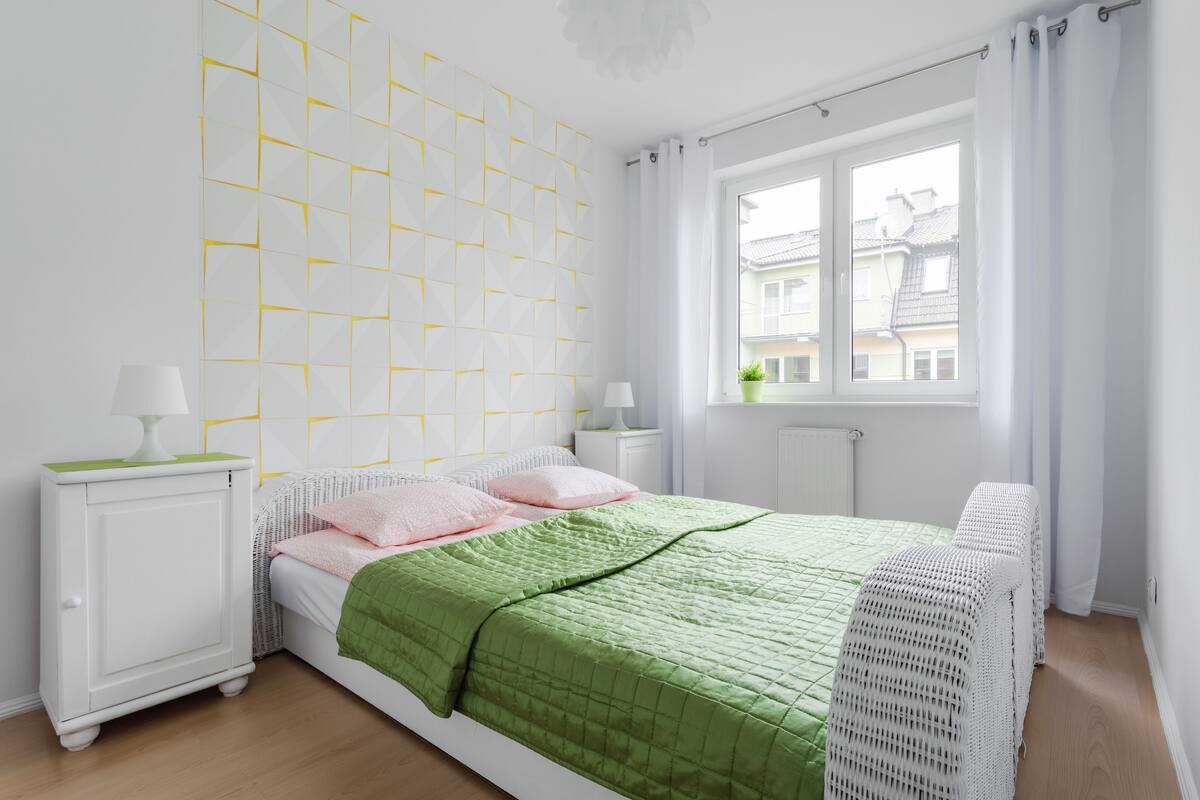A bedroom with a bed, two bedside tables, a window, and a wall with geometric patterns.