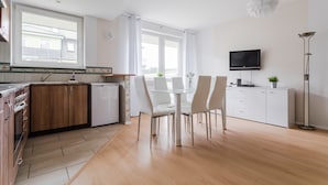 Una cocina moderna con armarios blancos, una mesa de comedor con sillas, un televisor montado en la pared y una lámpara de pie.