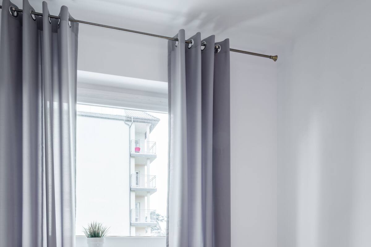 A bedroom with a wooden bed, grey curtains, a white radiator, and a window with a view of a building.