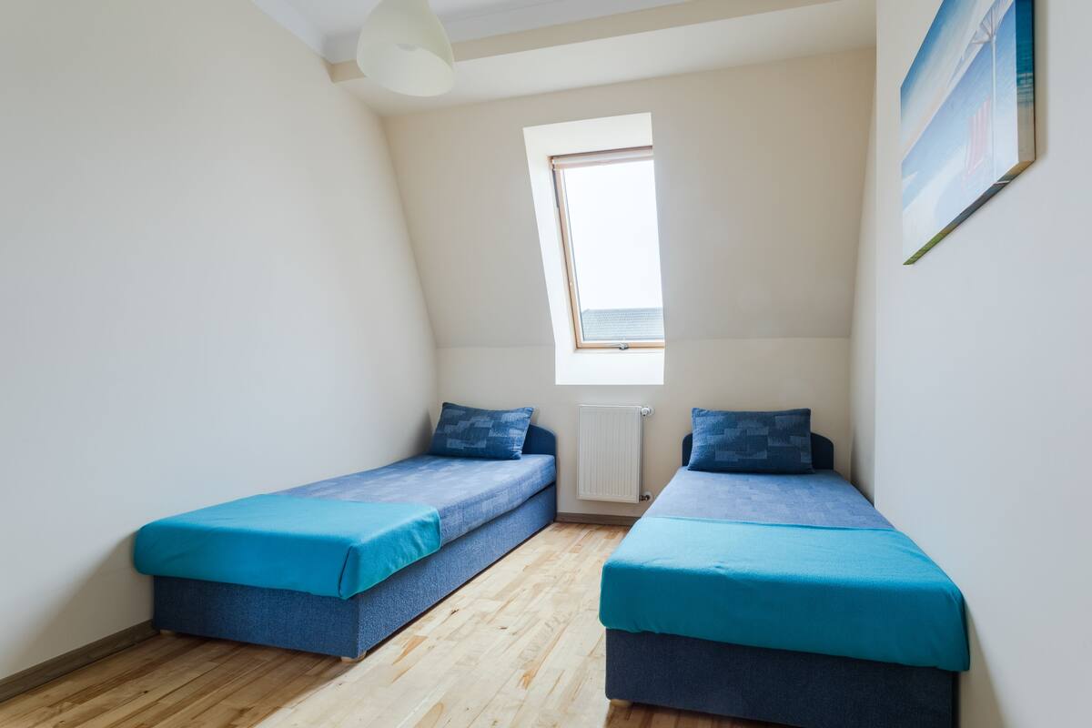A small, bright room with two single beds, a window, and a radiator.