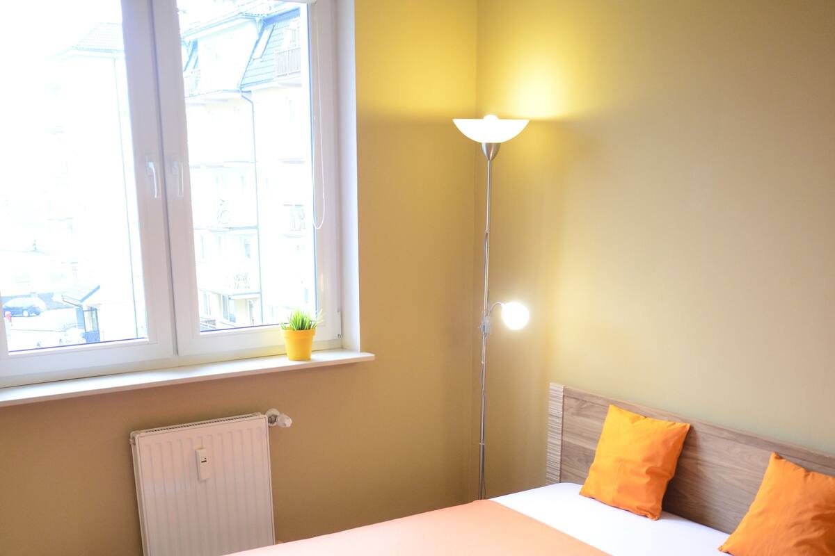 A bedroom with a bed, a window, a radiator, and a floor lamp.