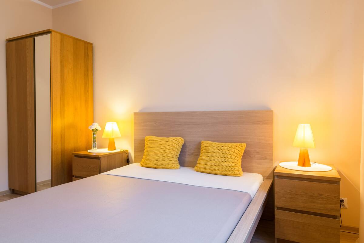A neatly made bed with two pillows, a wooden wardrobe, and two bedside tables with lamps.