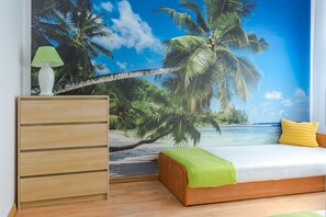 A bedroom with a beach mural, a wooden dresser, a bed with a green and yellow pillow, and a green lamp. - Apartamenty Baltyckie - Na Wydmie (Ustka)
