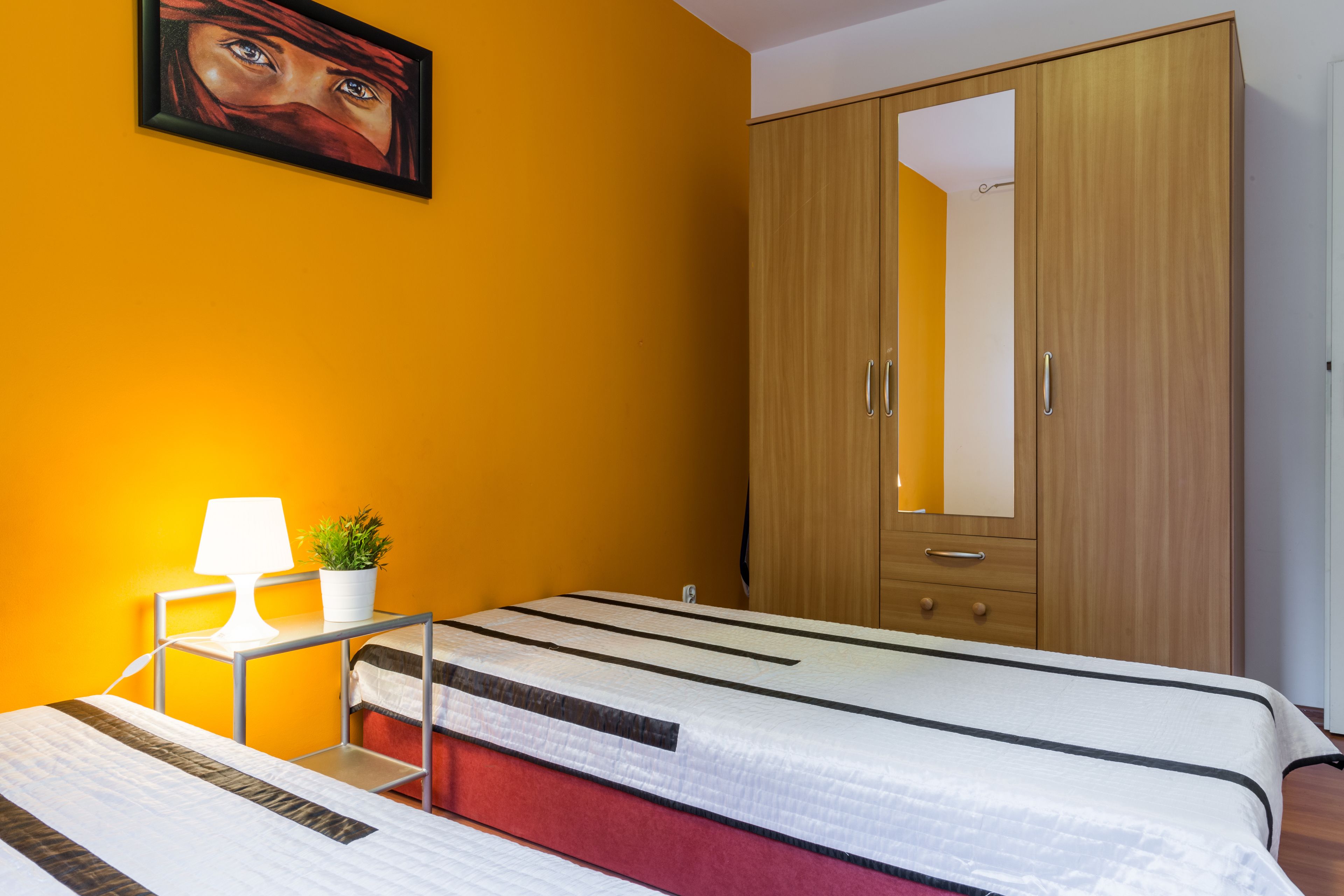 Une chambre avec un lit, une table de chevet avec une lampe, une plante en pot et une armoire.
