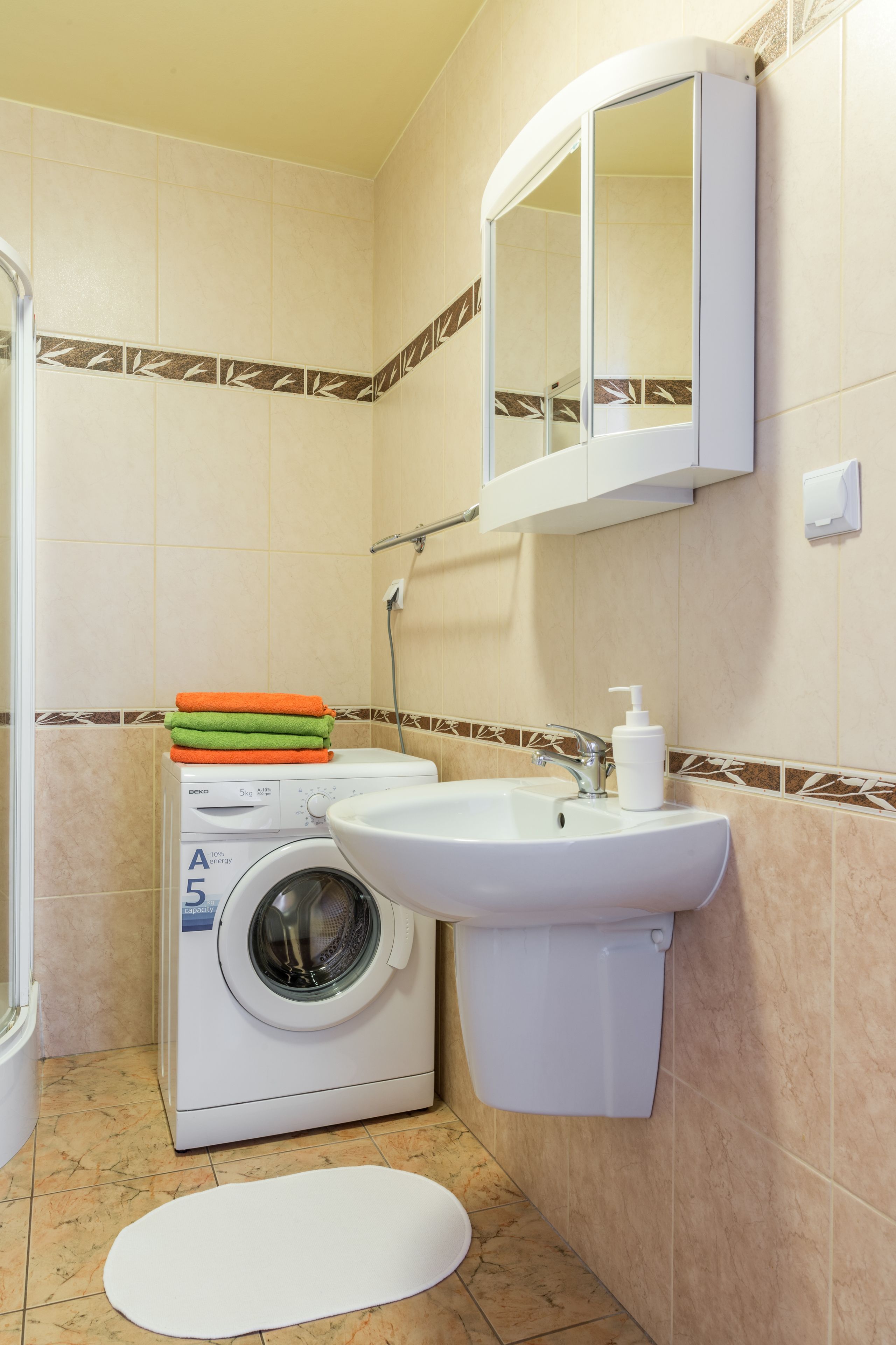 A compact bathroom with a washing machine, a sink, and a mirror.