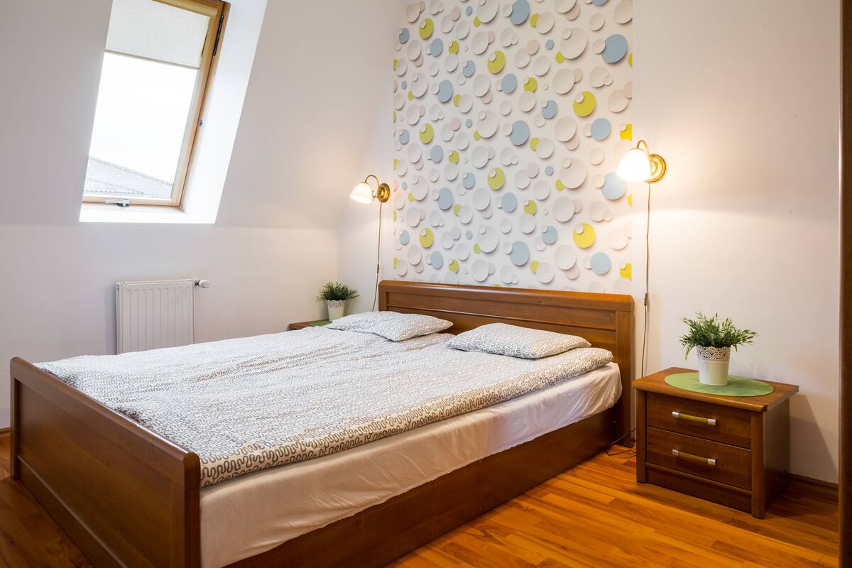 A bedroom with a wooden bed, two bedside tables with lamps, a radiator, and a wall with circular patterns.