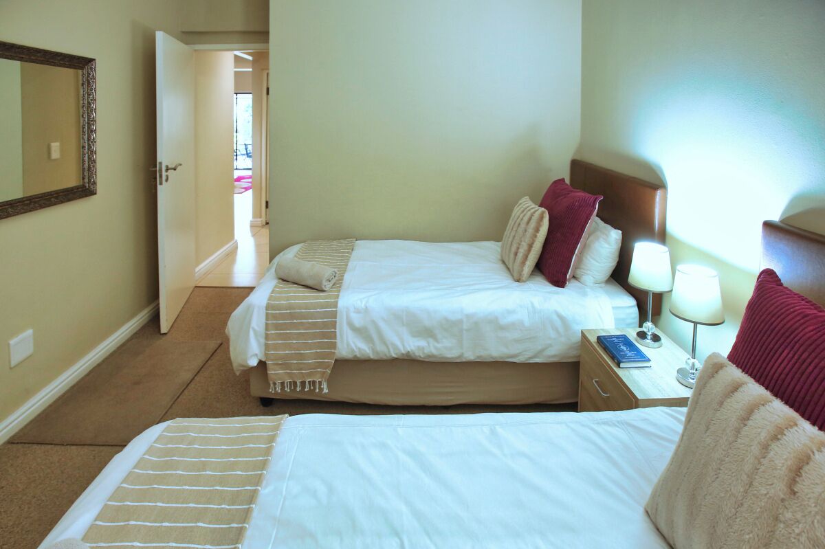 A hotel room with two beds, a nightstand with a lamp, and a mirror on the wall.