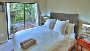 Un dormitorio con una cama grande, una mesita de noche, una lámpara y vistas a un jardín a través de un ventanal corredero.