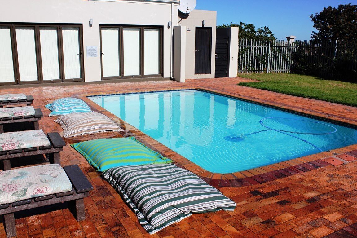 Una piscina rectangular con borde de baldosas, rodeada de sillas y cojines de descanso.