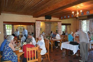 A dining area with wooden tables and chairs, a chandelier, and a speaker on the wall. - Old Halliwell Country Inn (Curry's Post)