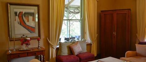 A living room with a sofa, a coffee table with fruit, a desk with a vase, and a window with curtains.