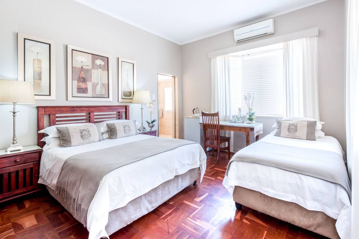 A hotel room with two beds, a wooden headboard, a desk with a chair, and framed artwork on the wall.